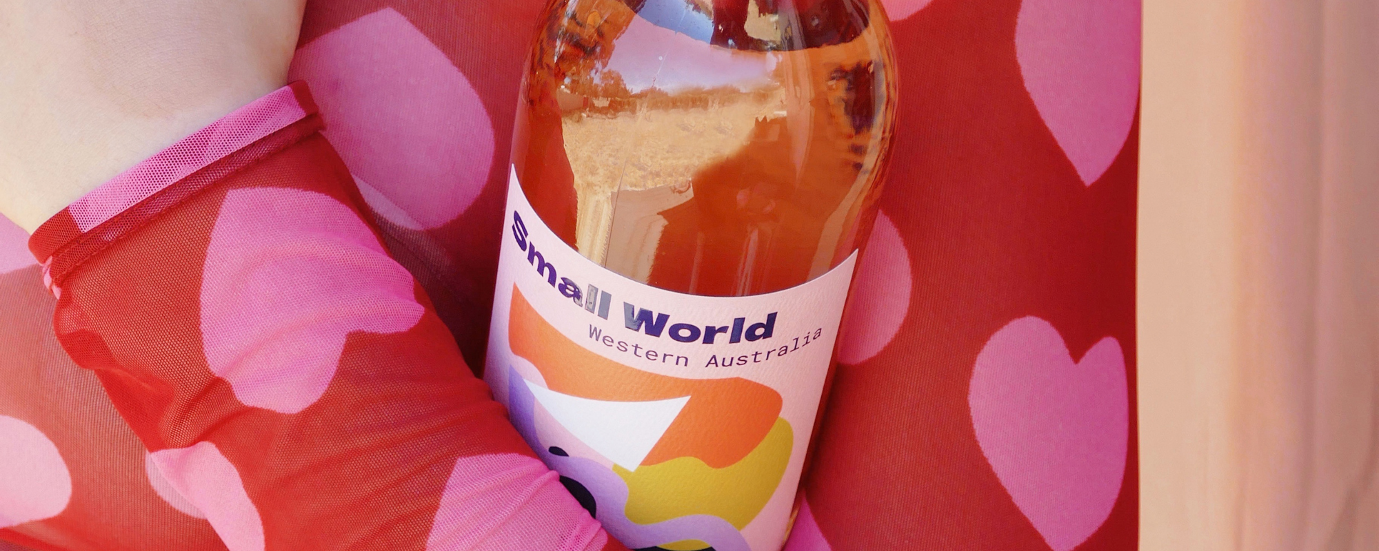 Small World wine bottle with a colourful label against a red shirt with pink hearts
